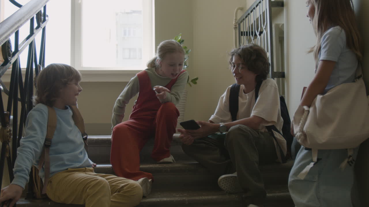 School children talking and looking at a smartphone on a staircase