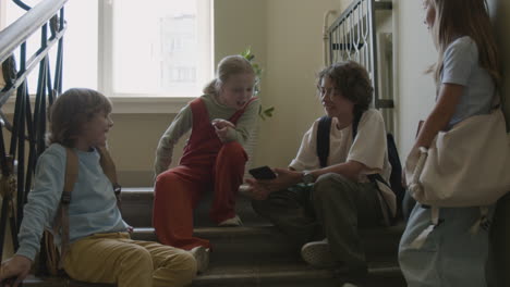 school children talking and looking at a smartphone on a staircase