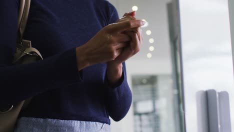 Mixed-race-businesswoman-in-face-mask-disinfecting-hands-upon-arrival-in-office