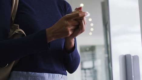 mujer de negocios de raza mixta con máscara facial desinfectando las manos a su llegada a la oficina
