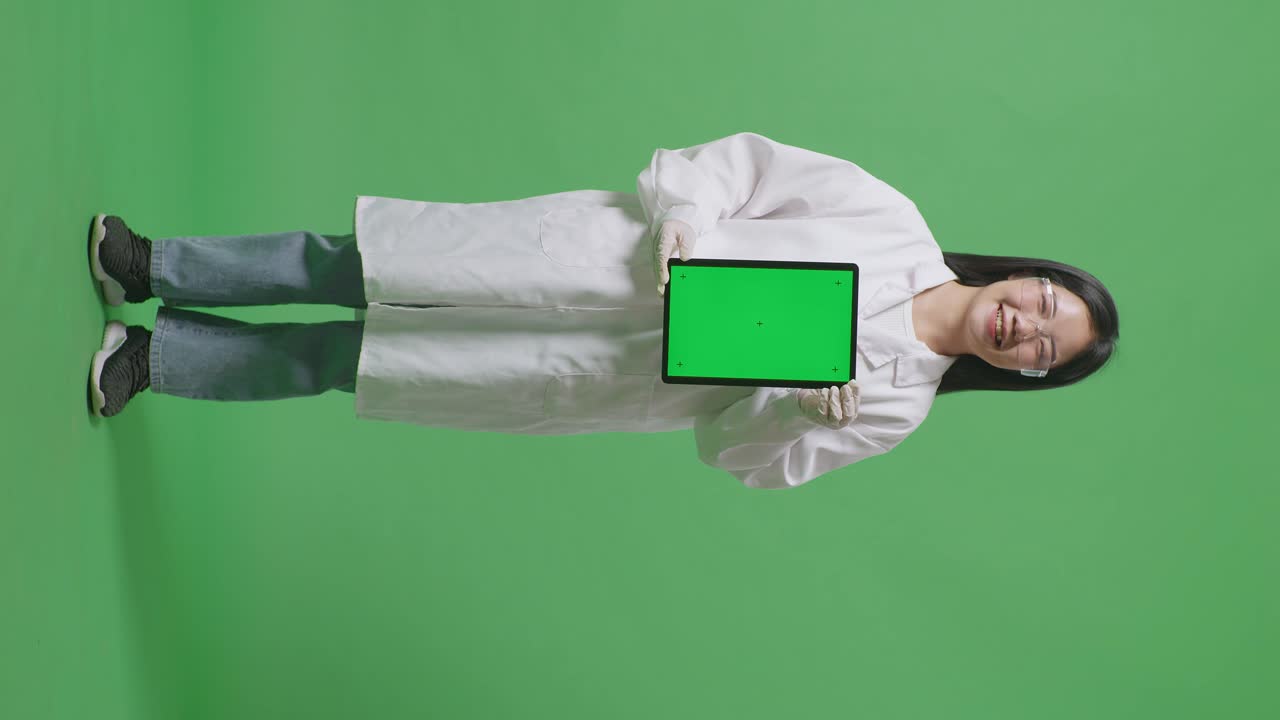cuerpo lleno de mujer científica asiática sonriendo y mostrando la tableta de pantalla verde a la cámara mientras estaba de pie en el fondo de la pantalla verde en el laboratorio