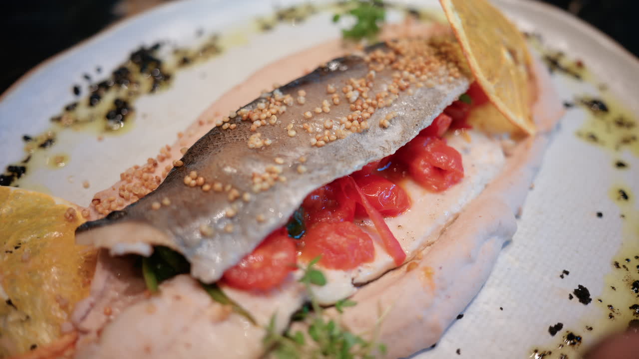 Primo piano di un filetto di pesce impiattato con cura, con salsa, fetta di limone ed erbe aromatiche