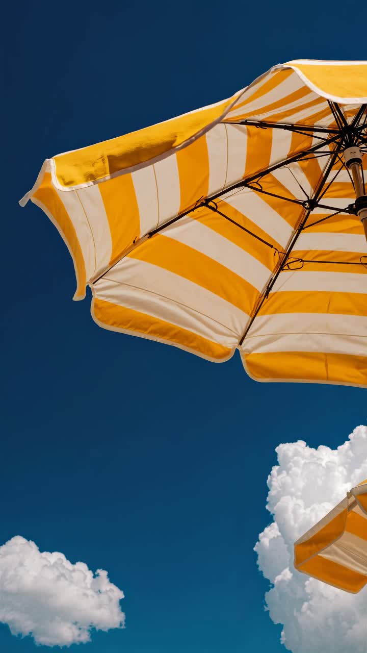 A low-angle video frame captures a vibrant blue sky with fluffy clouds and a yellow-striped