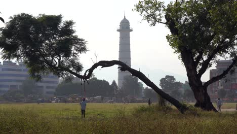 kathmandu, nepal - november 4, 2022: some young people playing on a swing on a tree in the shadow of the dharahara tower in kathmandu, nepal