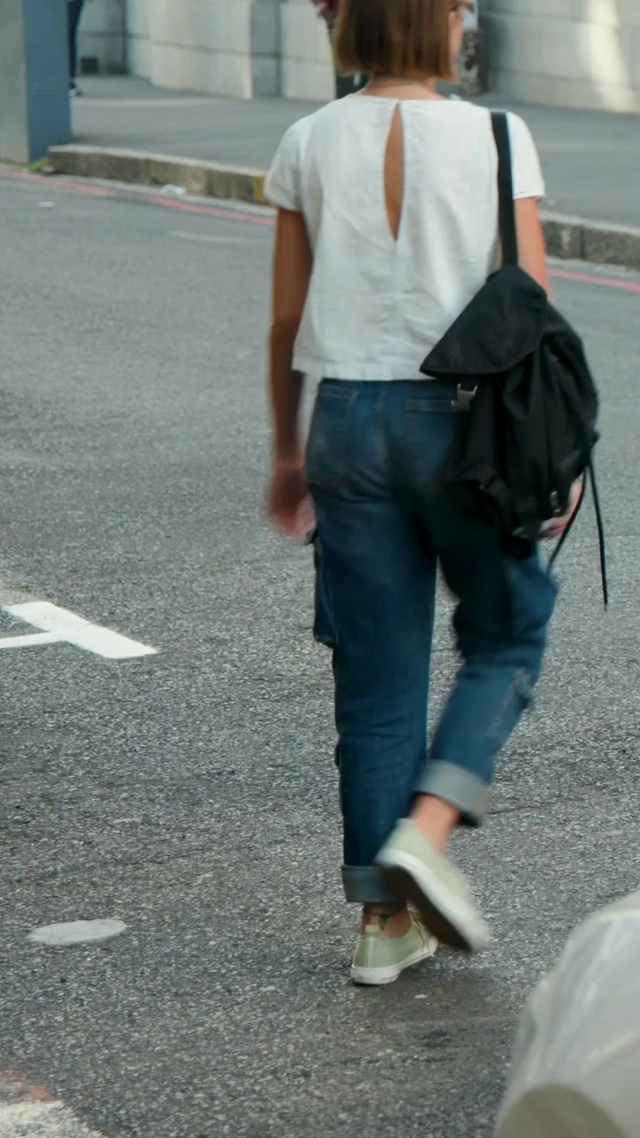 Vertical video: Entering from road, woman in white top crossing to sidewalk with pack, copy space