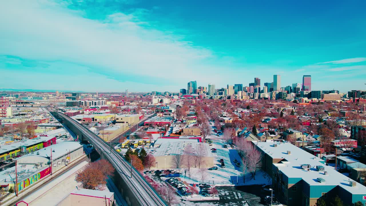 Winter aerial reveals Denver’s bustling downtown core, blanketed by snow against a backdrop of the majestic Rocky Mountains.