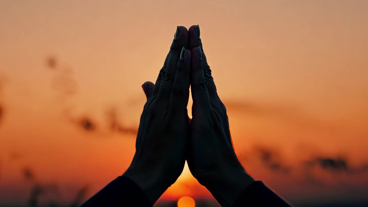 las manos siluetas se unen en un gesto de oración mientras el sol se pone en el fondo, creando una escena pacífica y meditativa