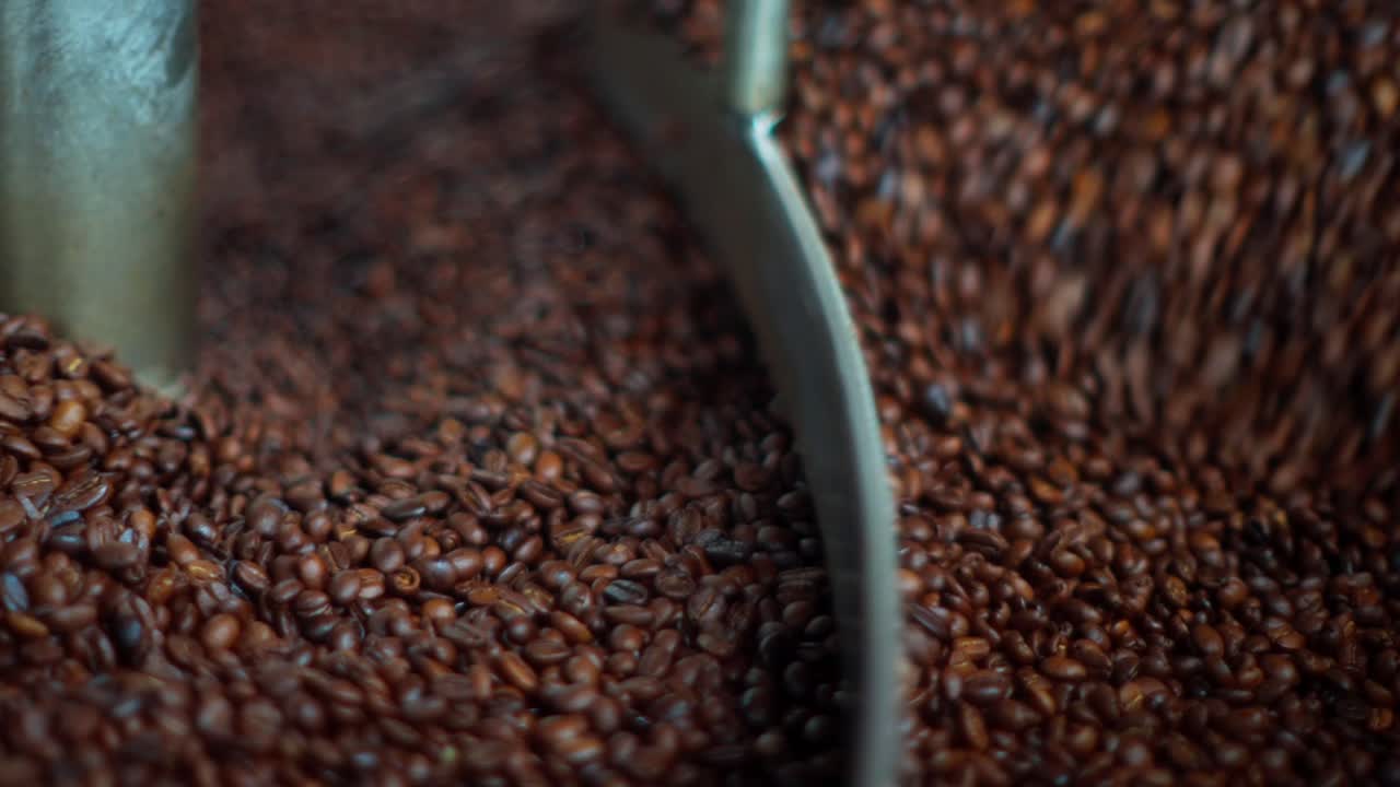 Chicchi di caffè tostati che si muovono all'interno di un tamburo di tostatura, sfondo ricco di texture, con statica media.