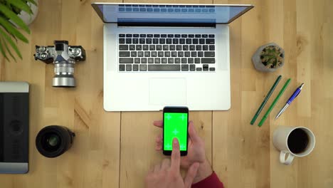 colocación plana de las manos del hombre usando el teléfono con pantalla verde en el lugar de trabajo