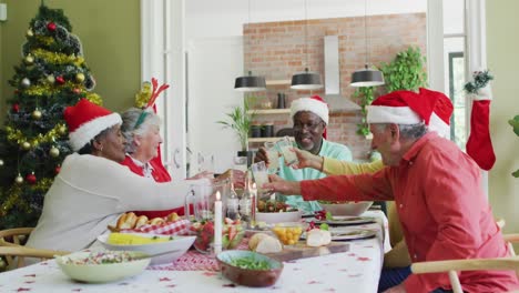 Animation-of-christmas-greetings-text-over-senior-diverse-friends-at-christmas-meal-table