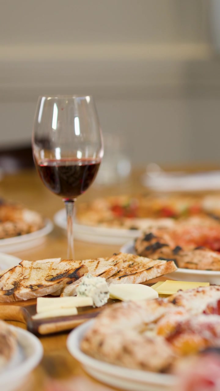 Primo piano di una mano che tiene del vino rosso accanto a una pizza con salamino piccante su un tavolo di ristorante.