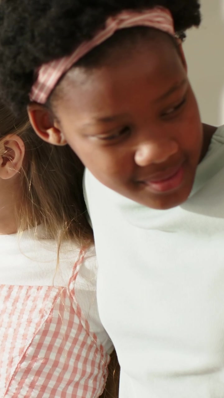 Vertical video: Glancing preteen girl leaning in and speaking at home, pale headband, gingham dress