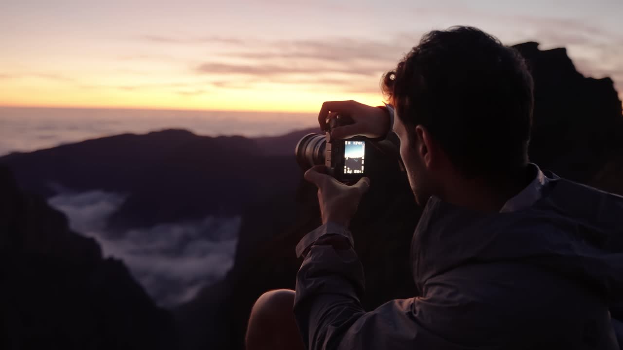 Man captures the mountain sunset through his camera viewfinder, focused on composing the perfect shot.