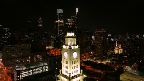 well lit white clock tower skyscraper among urban city skyline at night