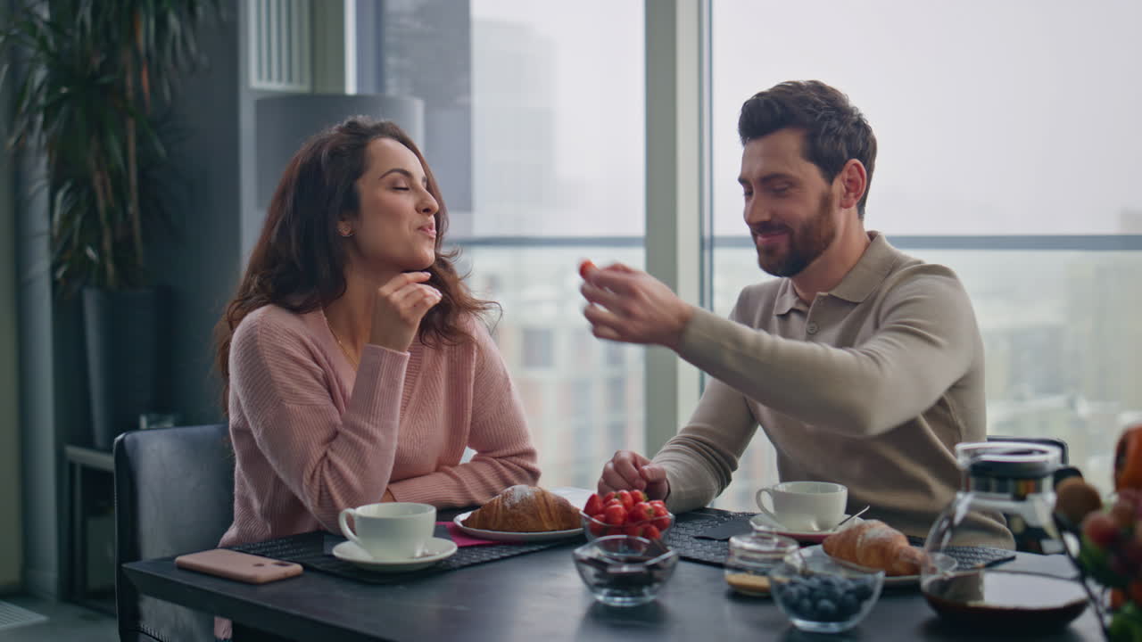 Primo piano di un uomo innamorato che nutre la moglie con una fragola in cucina. Colazione degli innamorati.