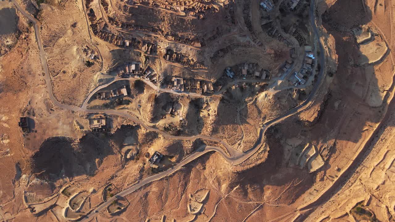 Stunning aerial shot of Chnenni, Tunisia, showcasing the unique desert landscape, ancient agricultural terraces, and a village nestled within the arid terrain.