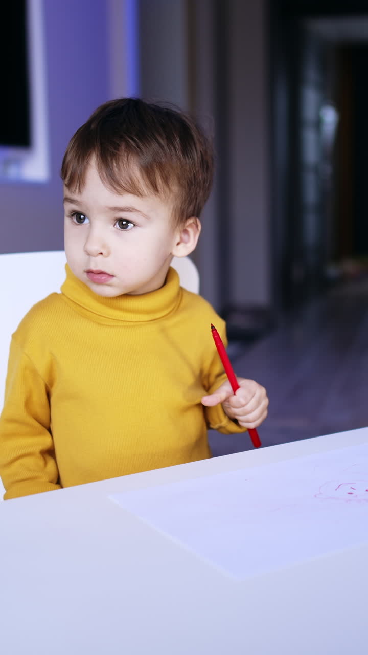 Un bambino carino che usa un pennarello. Un bambino con un maglione giallo smette di disegnare e guarda