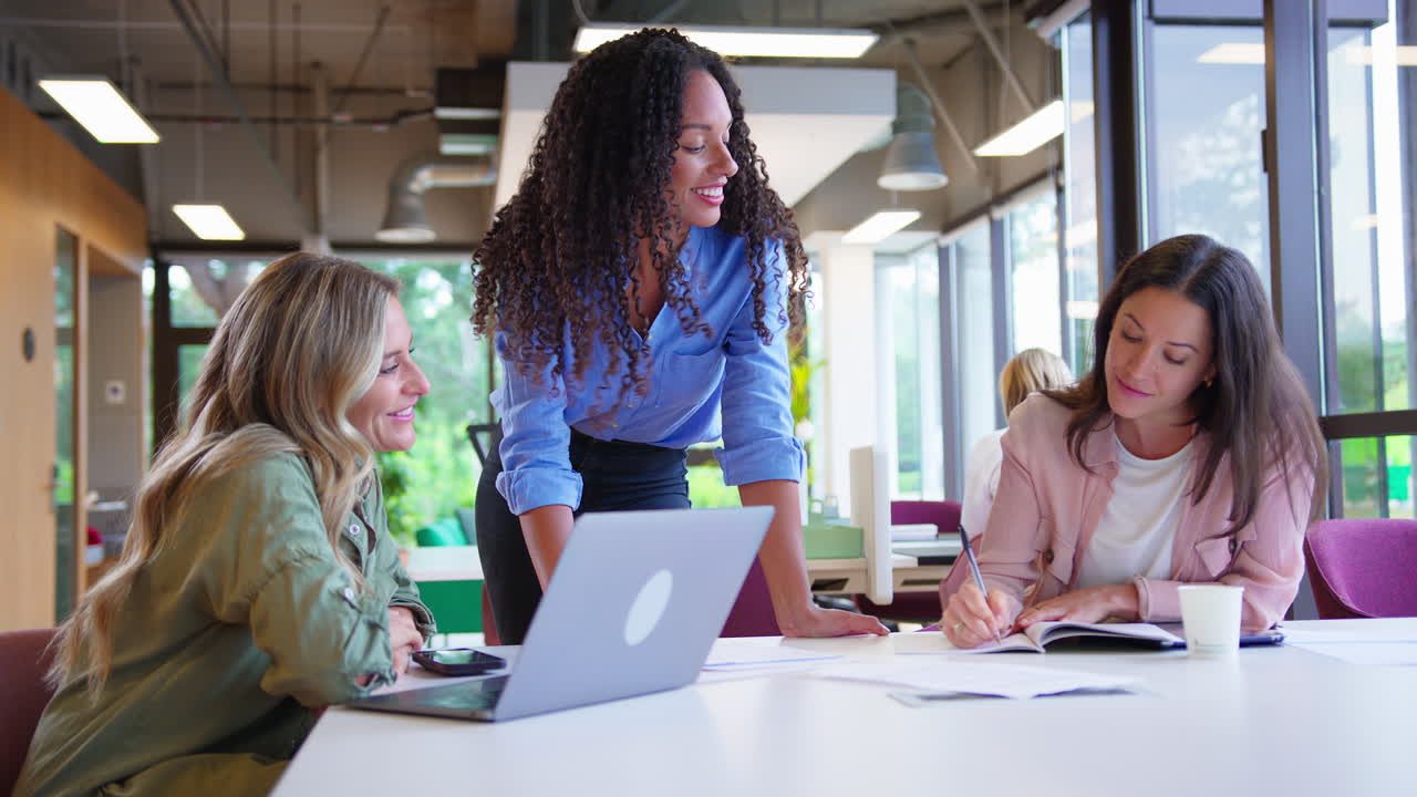 Multi-Cultural Female Business Team Sitting At Desk With Laptop In Office Collaborating On Project