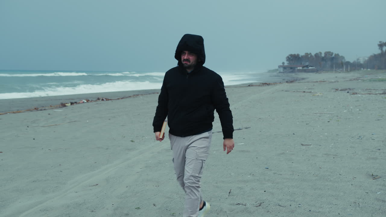 Man At The Sea In Winter Puts On His Hood To Protect From The Wind