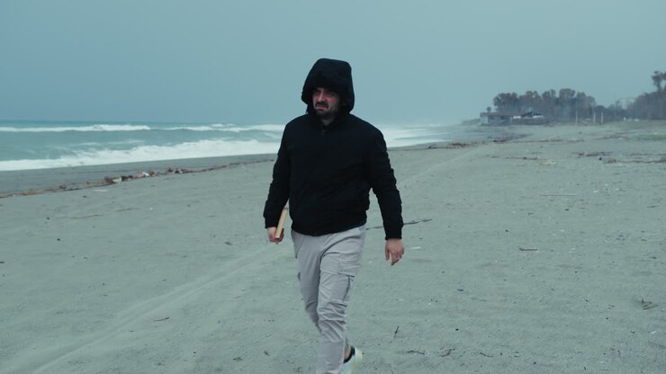 Uomo al mare in inverno si mette il cappuccio per proteggersi dal vento