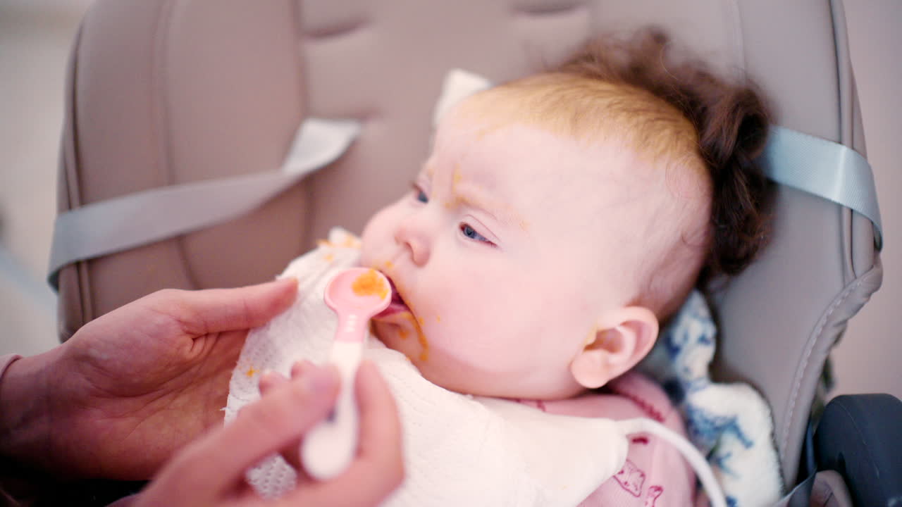 Close-up de um bebê sendo gentilmente alimentado com uma colher por um adulto.
