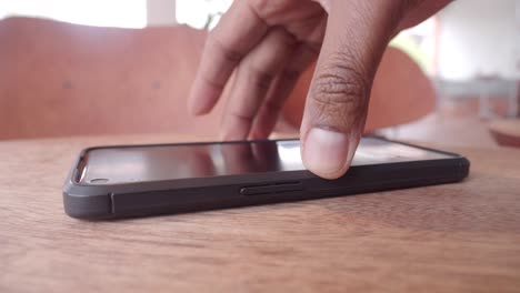 a smartphone on a wooden table with a hand and chairs in the background