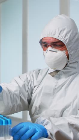 vertical video: scientist in sterile chemistry suit analysing blood sample from test tub