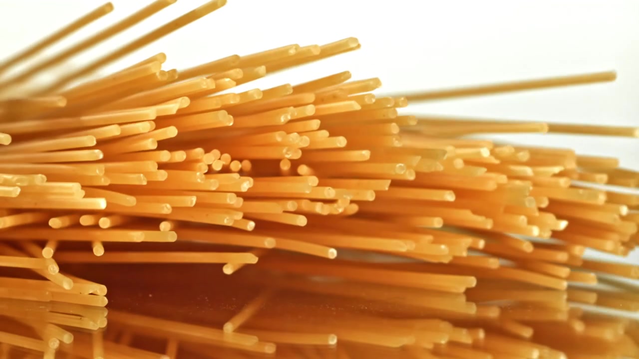 Spaghetti crudi che cadono e si dispongono su una superficie riflettente