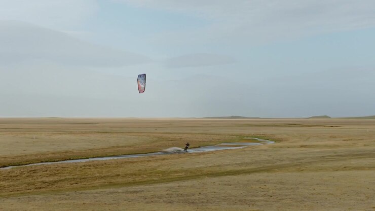 Kitesurfer som kjører i en svingete bekk over en enorm gyllen gresslette nedenfor Vatnajökull nær Höfn, Hornafjörður, sørøst på Island, droneopptak med sideveis sporing