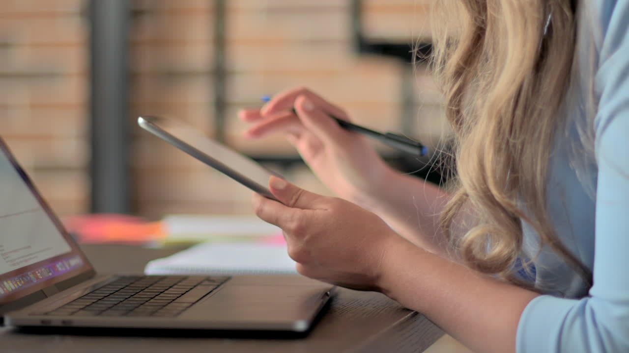 Woman in blue blazer working on a tablet and writing in a notebook at a desk in an office