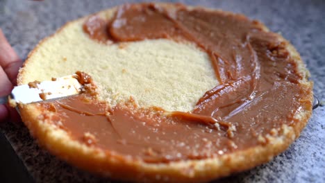 person spreading caramel on round sponge cake