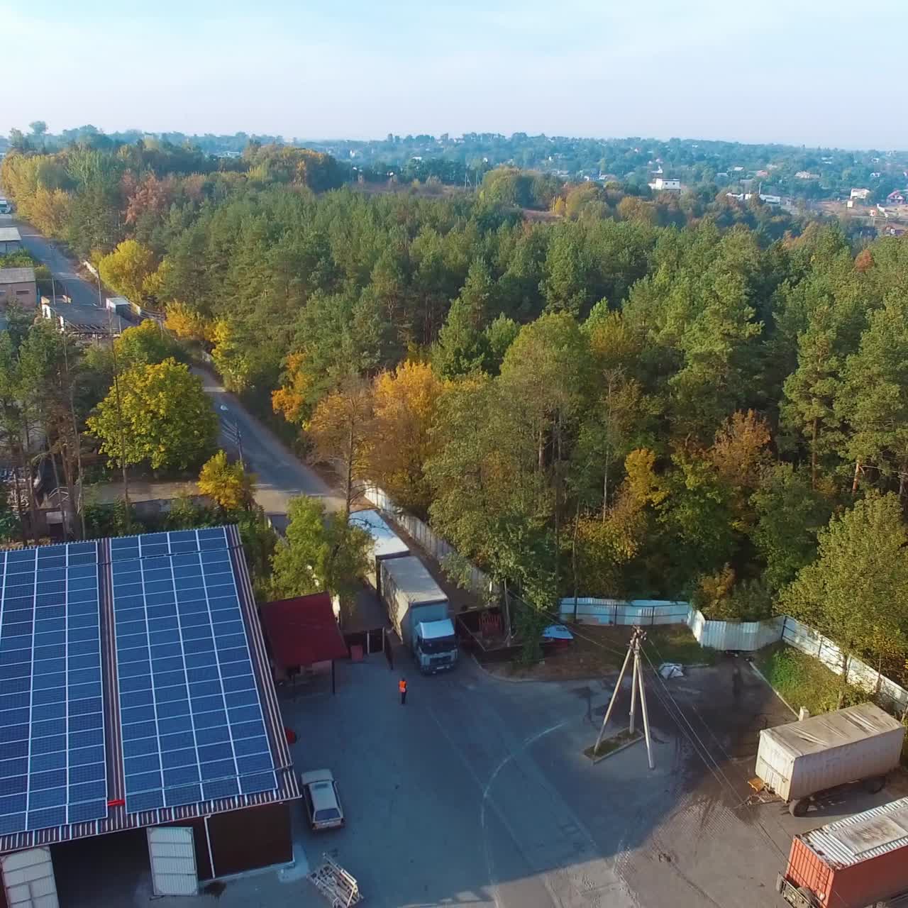 View from above on the road with trucks near green park. Building with solar energy panels in the countryside. Aerial view.