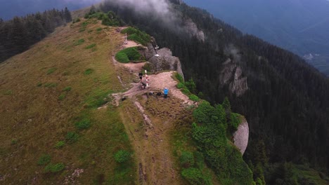 un dron circular aéreo disparó sobre un pico de montaña con 3 excursionistas admirando el amplio paisaje épico de un valle