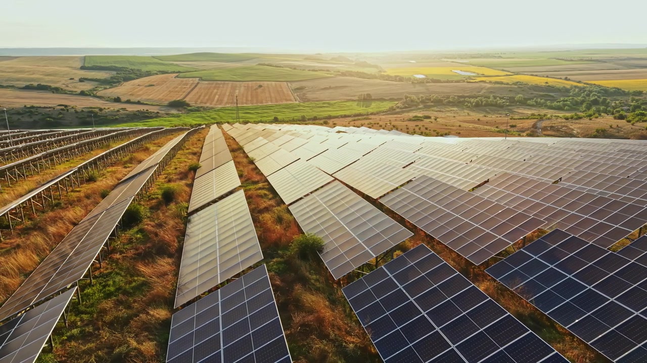 Solpaneler dækker land i en mark ved solnedgang med klar himmel og fjerne bakker i baggrunden, der viser indsatsen for vedvarende energi