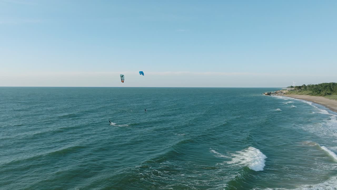 establecimiento de una vista aérea de un grupo de personas dedicadas al kitesurf, día soleado de verano, olas altas, deportes extremos, playa de karosta en el mar báltico, amplia toma de avión no tripulado avanzando