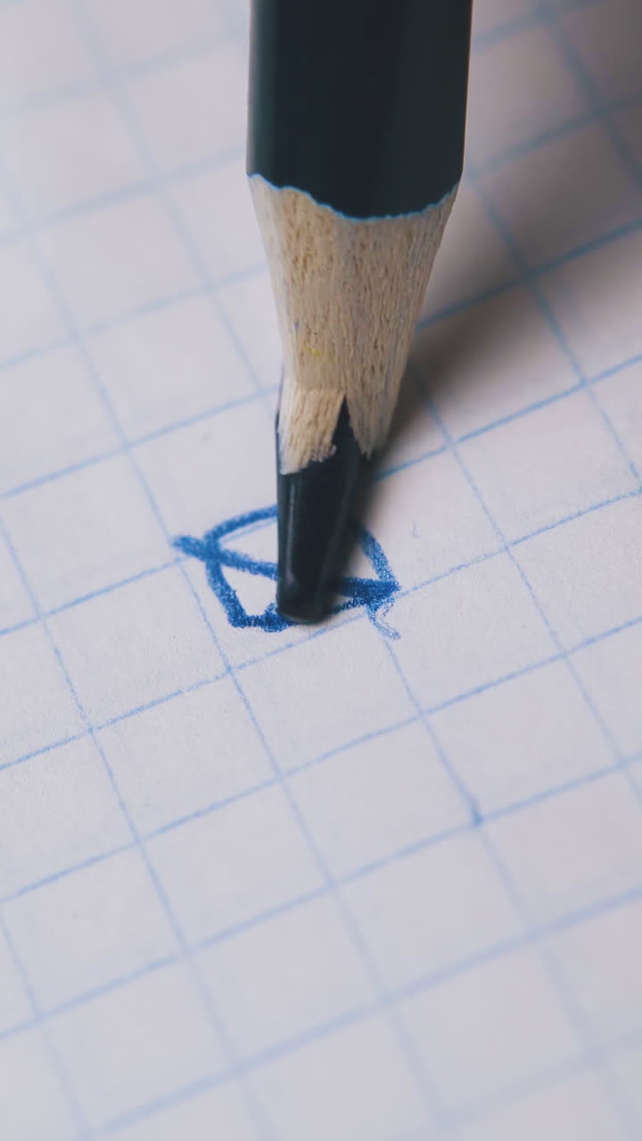 person draws picture and breaks slate of blue pencil on checkered paper sheet extreme close view
