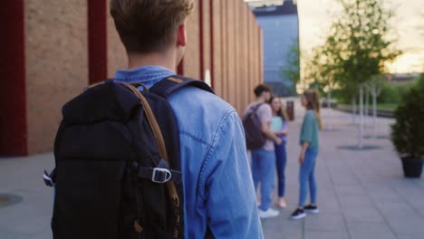 student walking and joining the group of caucasian students standing at university campus