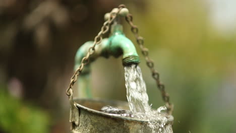 water falls in slowmotion in a garden from a diy outdoor faucet overflowing a rustic bucket into a barrel