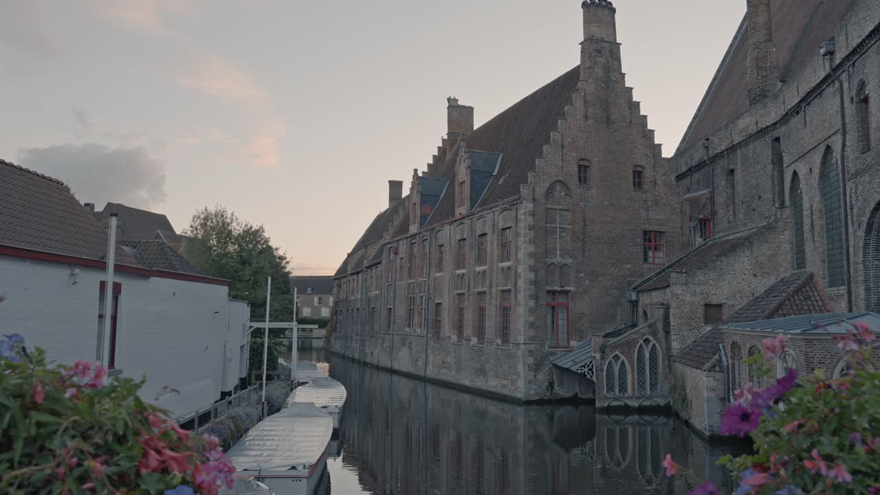 An atmospheric view at dusk in Bruges, Belgium, capturing a tranquil canal flanked by the imposing Gothic brick architecture of the Sint-Janshospitaal (Old St. John's Hospital)