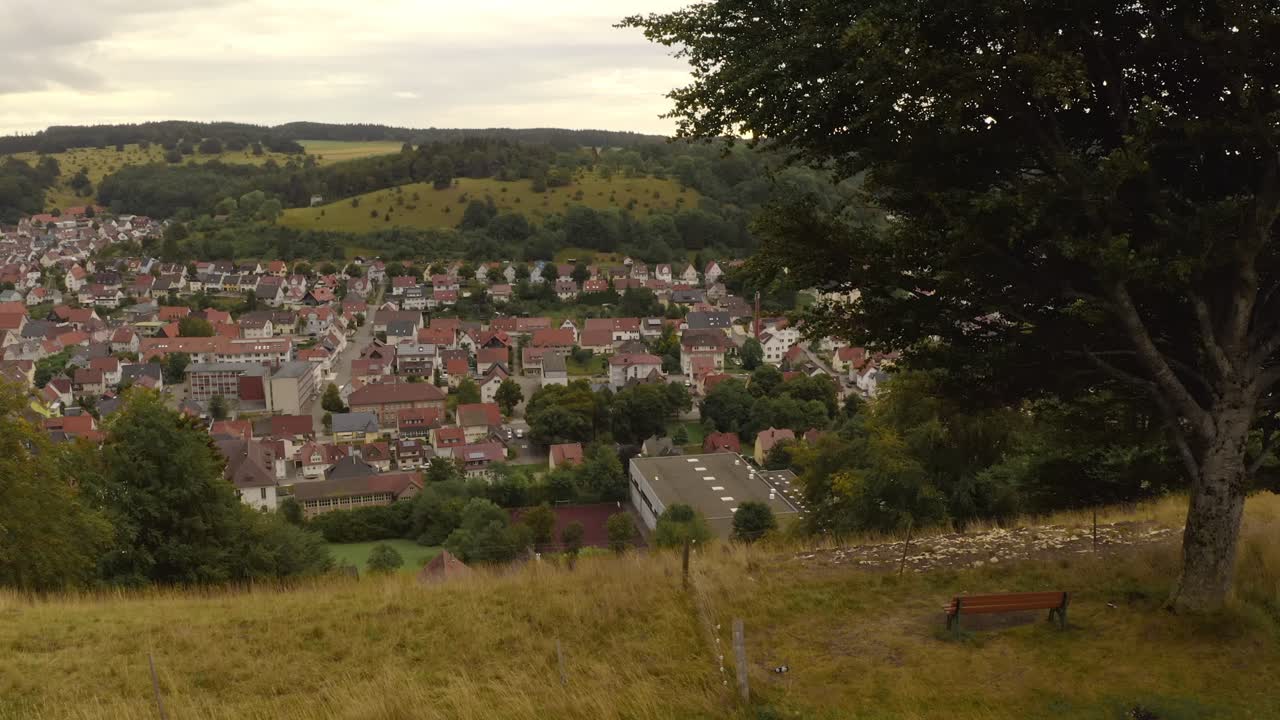Look up shot from a green meadow to a bench on a hill with the view at a part of a city in summer