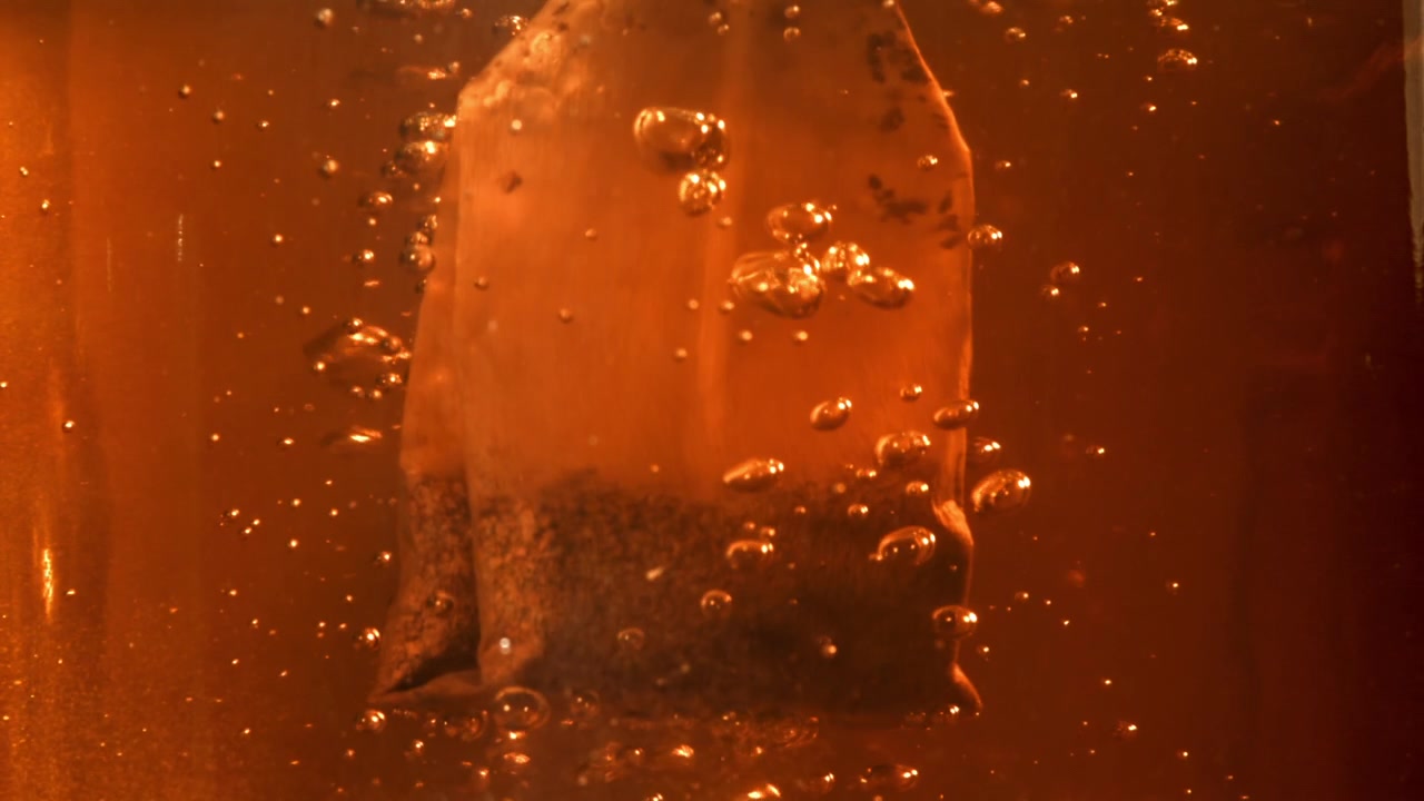 Primo piano di bustina di tè in infusione in acqua calda con bollicine