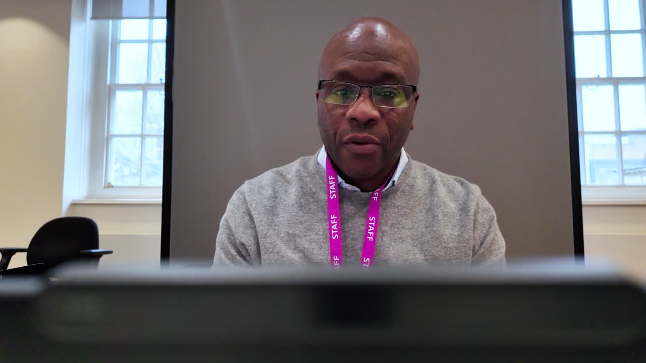 Office worker wearing a staff badge, focused on using a laptop while seated in a modern office pod during the day