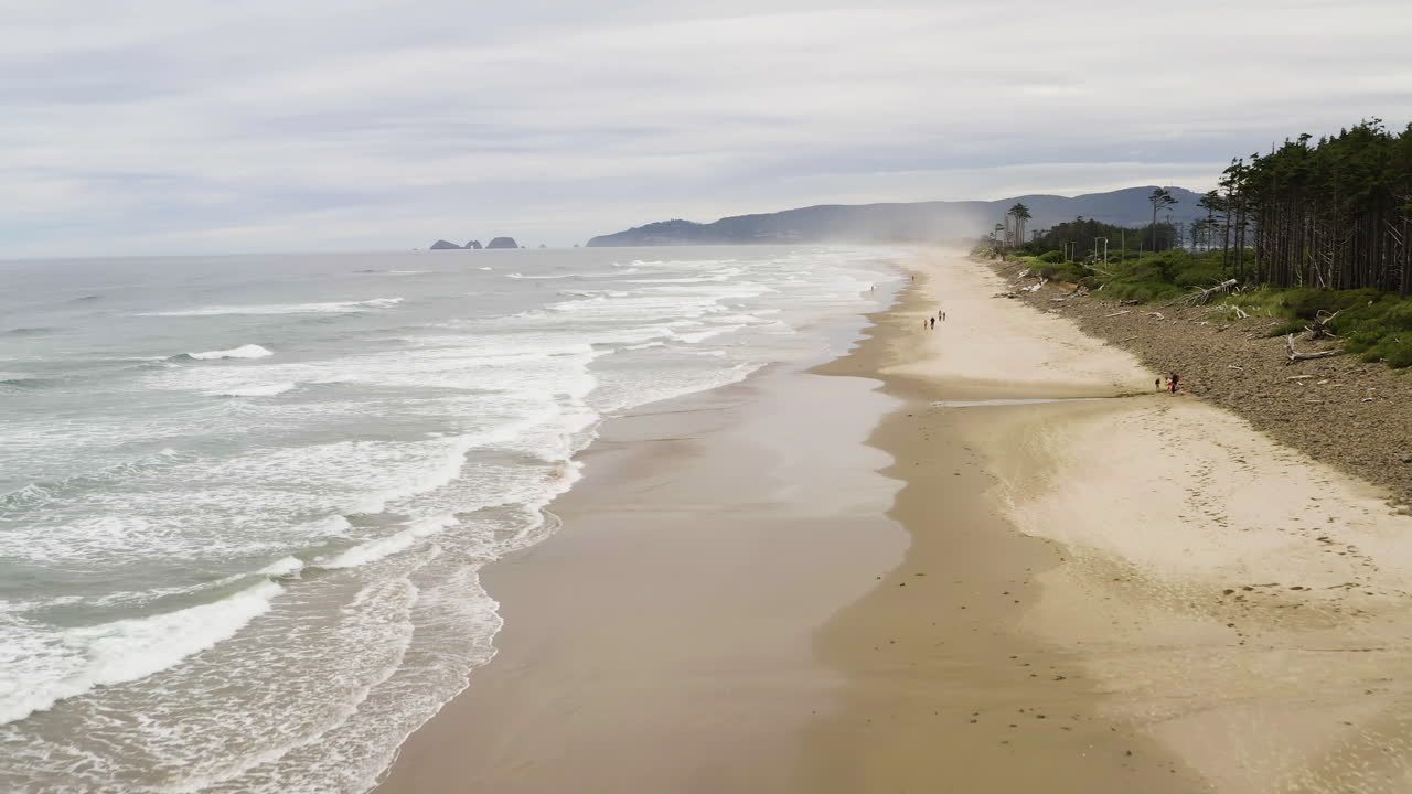 Dolly aéreo ao longo de ondas suaves quebrando em uma ampla praia de areia de Cape Lookout, Oregon