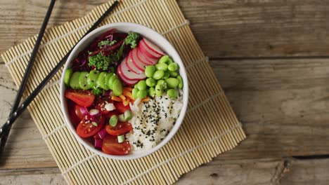 Composition-of-bowl-of-rice-and-vegetables-with-chopsticks-on-wooden-background