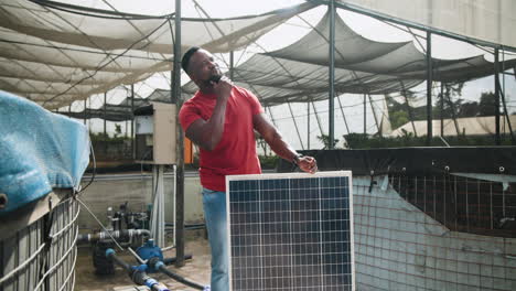 man in red shirt installing solar panel at greenhouse, focusing on renewable energy