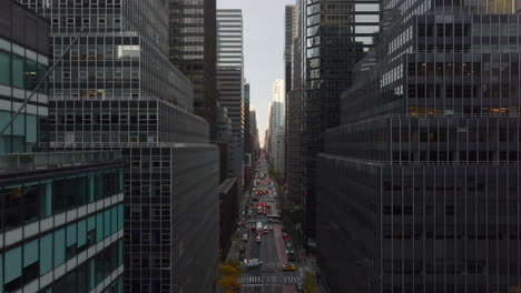 Fly-above-wide-long-and-straight-avenue-in-downtown.-Modern-tall-skyscrapers-standing-around.-Manhattan,-New-York-City,-USA