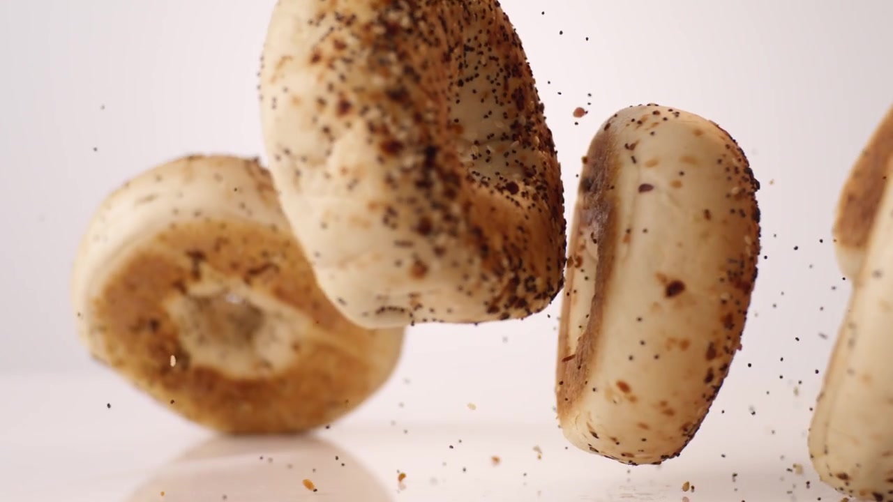 Everything-seeded savory bagels dropping and bouncing across white seamless backdrop in high speed slow motion. brunch menu reels, hotel buffet posts, savory breakfast videos.