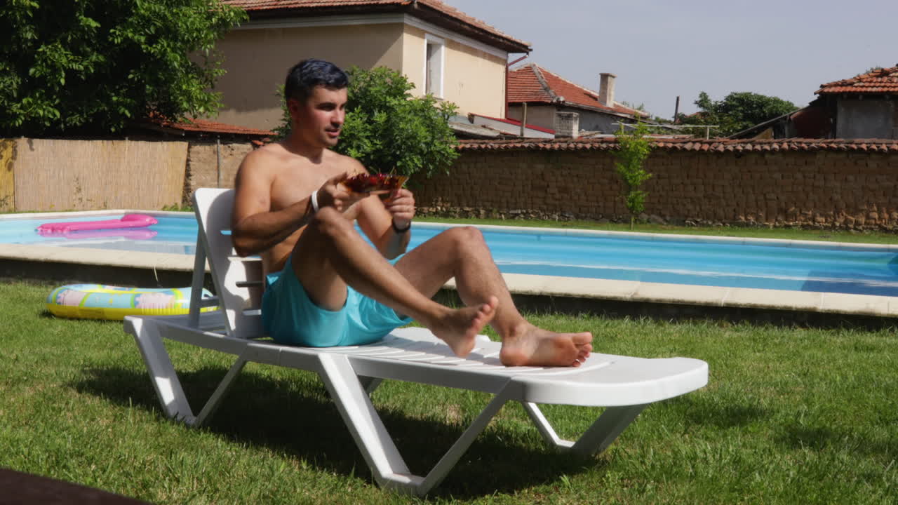 Man in swim trunks walks to lounge chair by a pool in a backyard on a sunny day