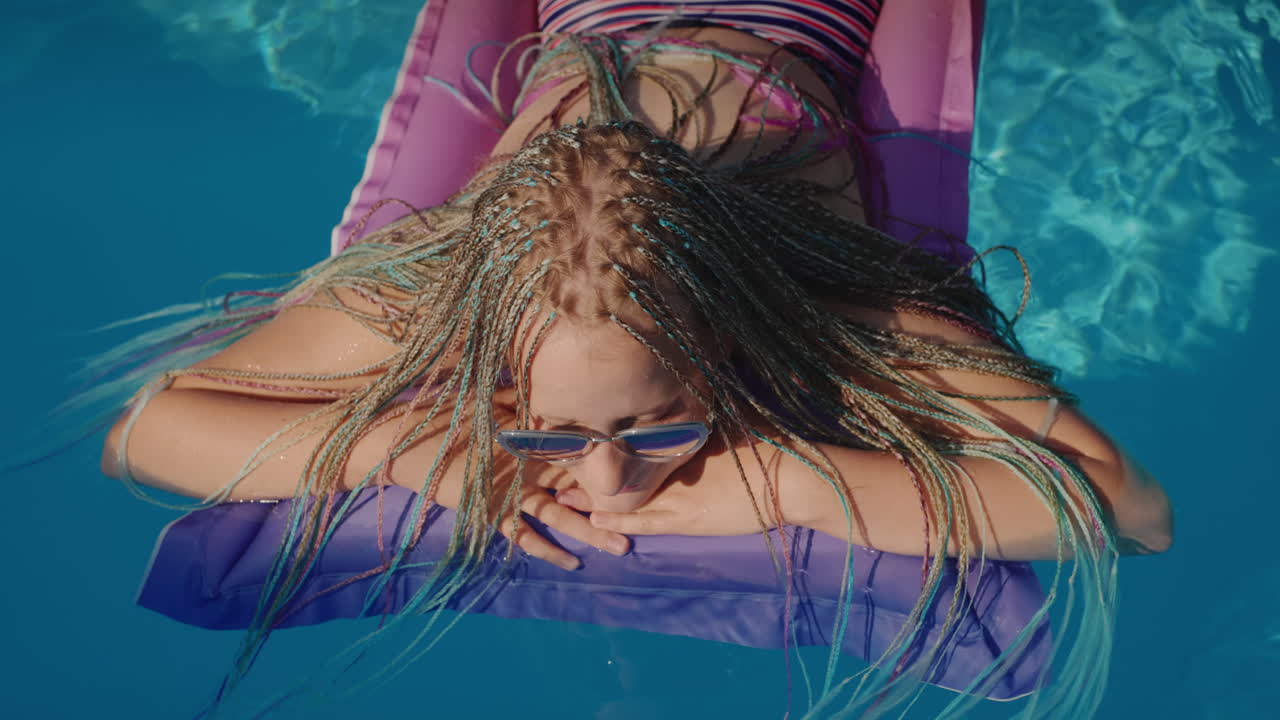 Top view: A child with afro pigtails swims on an inflatable mattress in the pool, resting and enjoying the rest.