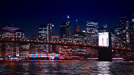 the brooklyn bridge beautifully lit at night. view from the waterscape of the east river. modern dazzling skyline of new york at backdrop